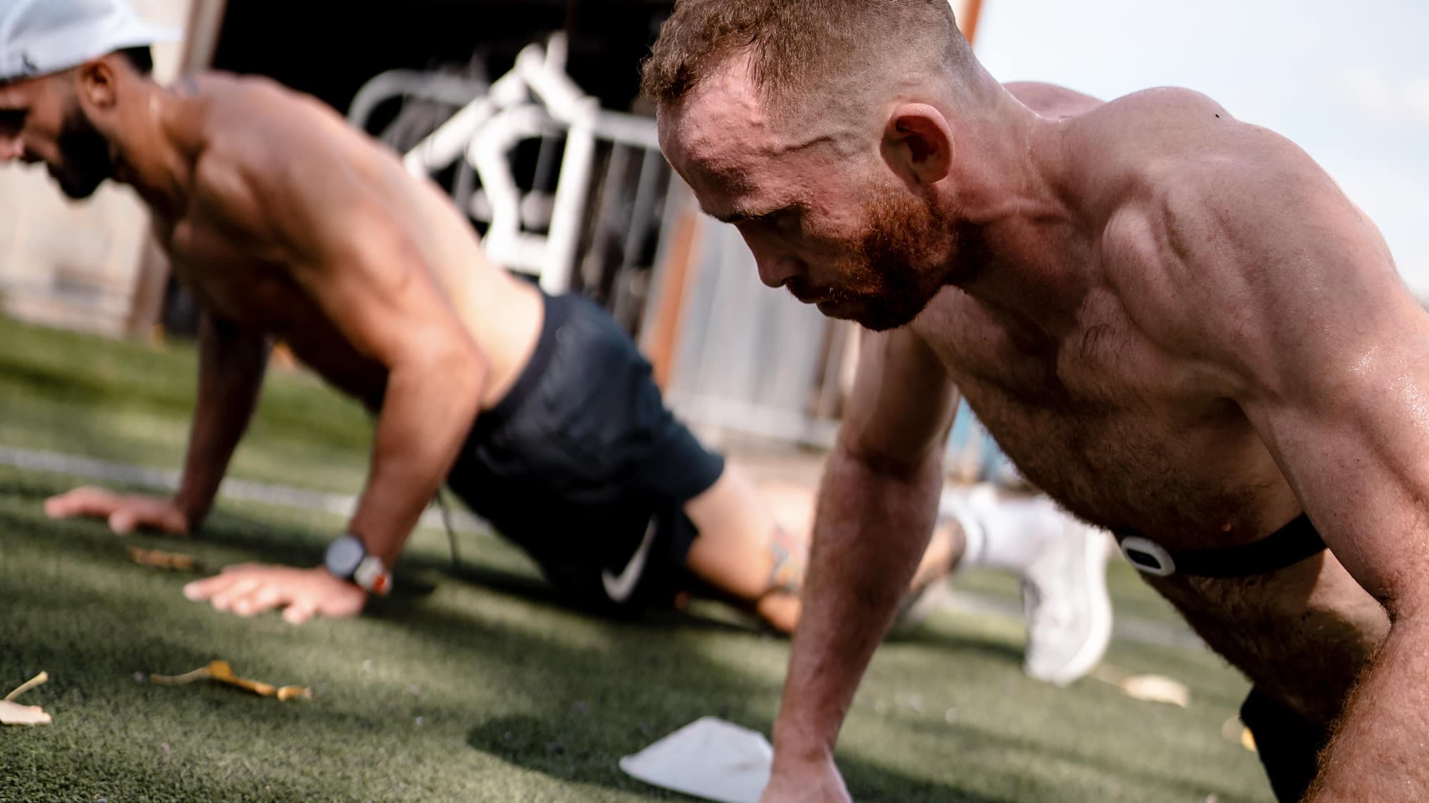 Two athletes in the bottom of a burpee broad jump on turf