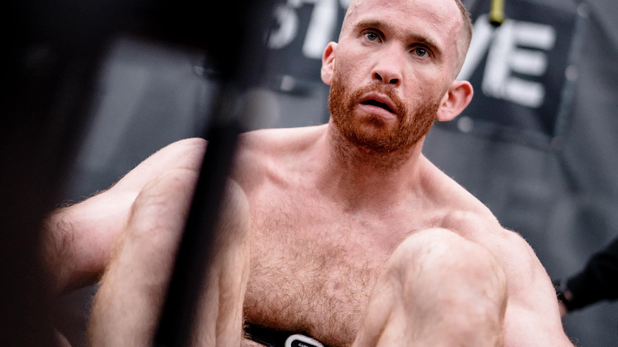Ben Sutherland mid-effort on the rower, seen across the flywheel