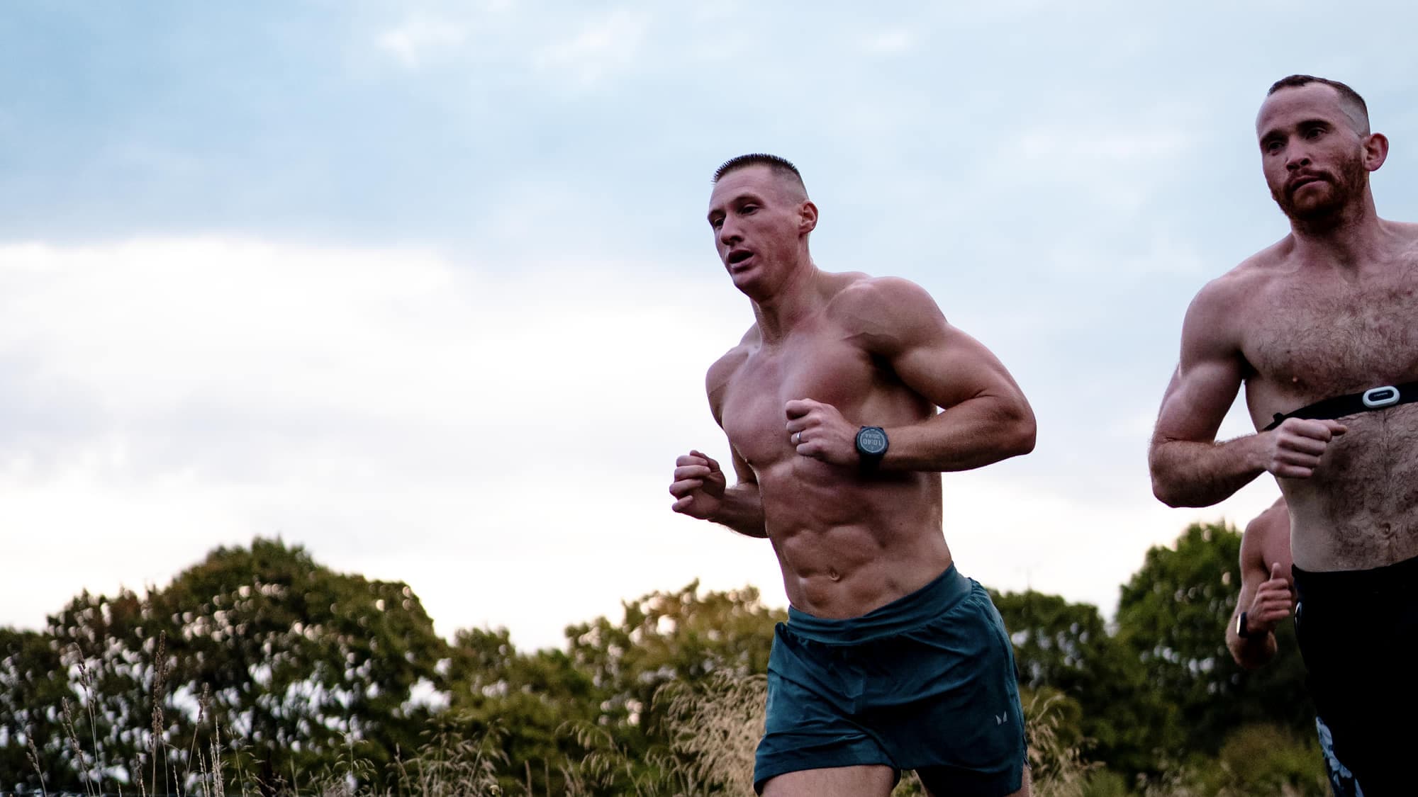 Two athletes running uphill against an open sky