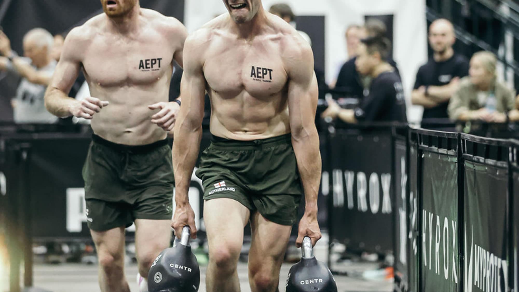 Two athletes carrying kettlebells down the farmers carry lane