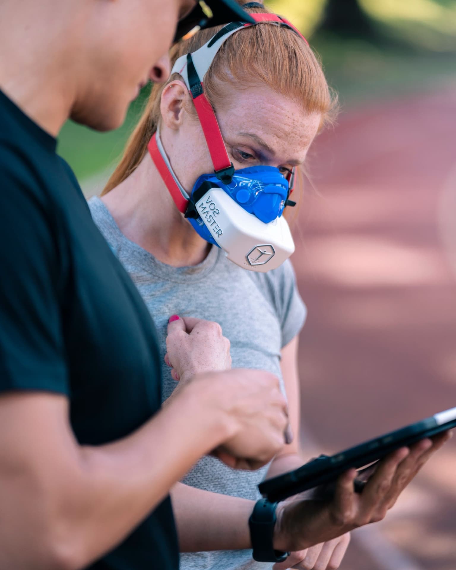 A coach recording data while an athlete completes a VO2 max test wearing a breathing mask